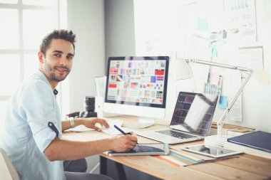 İnternette çalışırken bilgisayarın ve dizüstü bilgisayarın önünde grafik stüdyosunda oturan genç tasarımcının portresi.