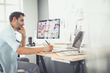 İnternette çalışırken bilgisayarın ve dizüstü bilgisayarın önünde grafik stüdyosunda oturan genç tasarımcının portresi.
