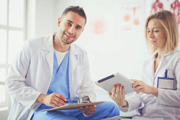 Hezký doktor je mluvit s mladou ženou lékaře a dělat si poznámky, zatímco sedí ve své kanceláři. — Stock fotografie