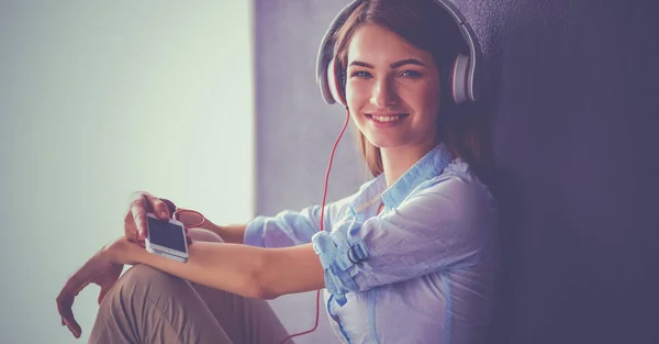 Smiling girl with headphones sitting on the floor near wall