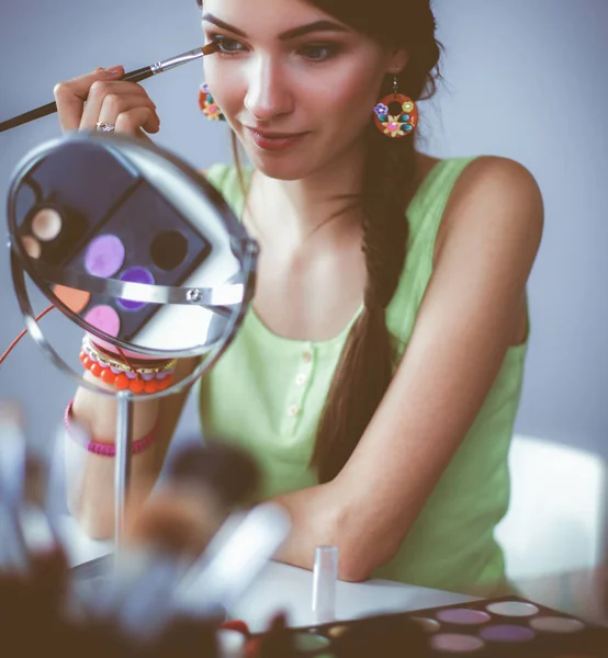 Joven hermosa mujer haciendo maquillaje cerca del espejo, sentado en el escritorio — Foto de Stock