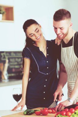 Sebze doğrayan genç bir adam ve mutfakta dizüstü bilgisayarı olan bir kadın.