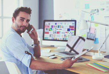 İnternette çalışırken bilgisayarın ve dizüstü bilgisayarın önünde grafik stüdyosunda oturan genç tasarımcının portresi.