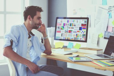 İnternette çalışırken bilgisayarın ve dizüstü bilgisayarın önünde grafik stüdyosunda oturan genç tasarımcının portresi.