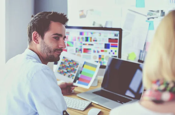 Retrato del joven diseñador sentado en el estudio gráfico frente a la computadora portátil y el ordenador mientras trabaja en línea. — Foto de Stock