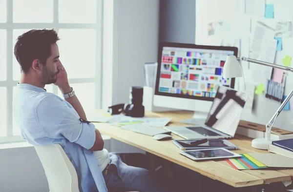 Porträt eines jungen Designers, der im Grafikstudio vor Laptop und Computer sitzt, während er online arbeitet. — Stockfoto