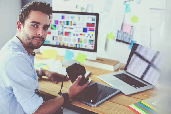 Retrato del joven diseñador sentado en el estudio gráfico frente a la computadora portátil y el ordenador mientras trabaja en línea. — Foto de Stock