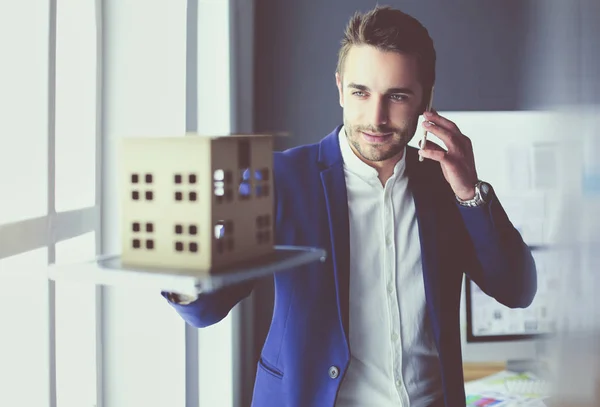 Homme d'affaires tenant maison miniature à portée de main debout dans le bureau . — Photo