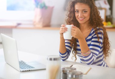 kahve fincanı ve dizüstü evde mutfakta gülümseyen genç kadın