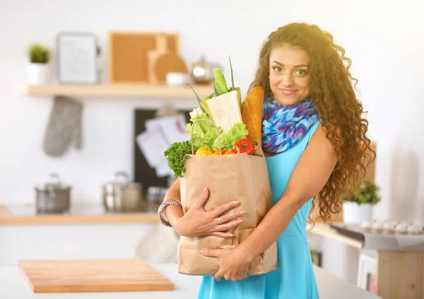 Ung kvinna som håller i matkassen med grönsaker Står i köket. — Stockfoto