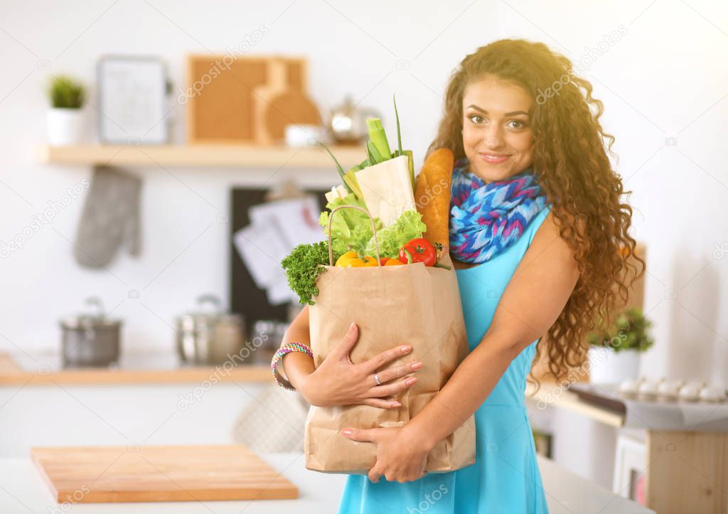 Young woman holding grocery shopping bag with vegetables Standing in the kitchen. 