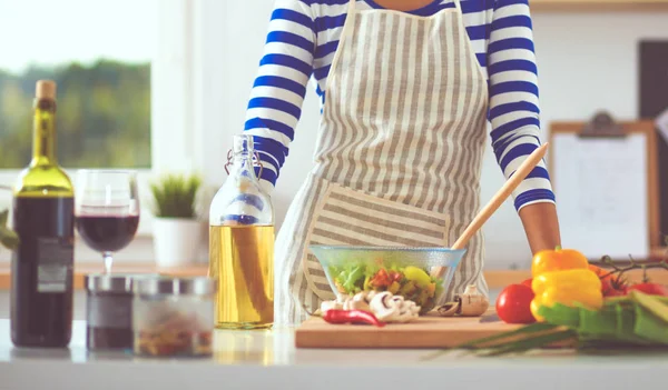 Gülümseyen kadın mutfakta salata hazırlıyor.