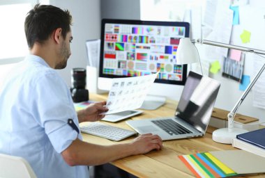 İnternette çalışırken bilgisayarın ve dizüstü bilgisayarın önünde grafik stüdyosunda oturan genç tasarımcının portresi.