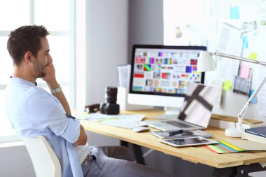 İnternette çalışırken bilgisayarın ve dizüstü bilgisayarın önünde grafik stüdyosunda oturan genç tasarımcının portresi.