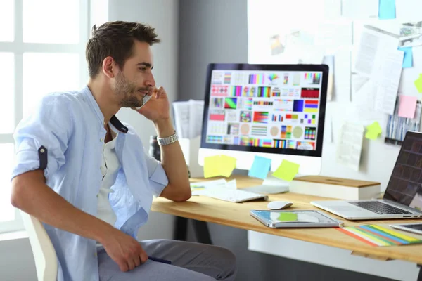 Retrato del joven diseñador sentado en el estudio gráfico frente a la computadora portátil y el ordenador mientras trabaja en línea. — Foto de Stock