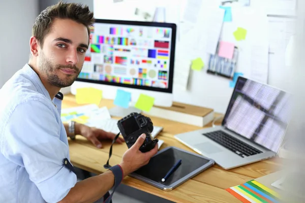 Retrato del joven diseñador sentado en el estudio gráfico frente a la computadora portátil y el ordenador mientras trabaja en línea. — Foto de Stock