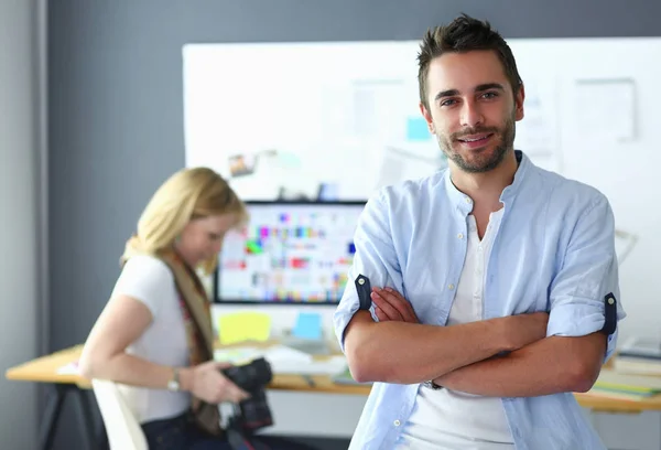 Retrato del joven diseñador delante de la computadora portátil y el ordenador mientras trabaja. Asistente usando su móvil en segundo plano . —  Fotos de Stock