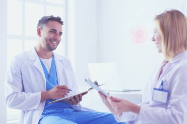 Yakışıklı doktor genç bayan doktorla konuşuyor ve ofisinde otururken notlar alıyor..