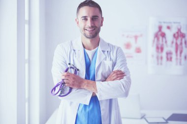 Genç ve kendinden emin erkek doktor portresi tıp ofisinde duruyor..