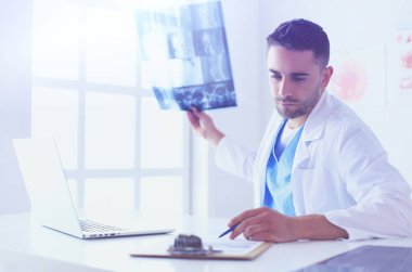 Yakışıklı doktor genç bayan hastasıyla konuşuyor ve ofisinde otururken notlar alıyor..