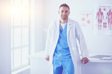 Genç ve kendinden emin erkek doktor portresi tıp ofisinde duruyor..