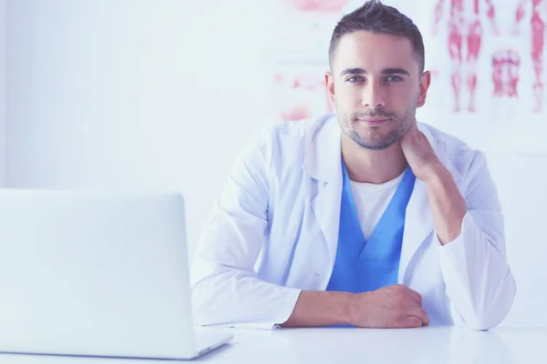 Портрет лікаря-чоловіка з ноутбуком, що сидить за столом у медичному кабінеті . — стокове фото