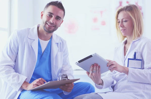 El guapo doctor está hablando con una joven doctora y tomando notas mientras está sentado en su consultorio.. — Foto de Stock