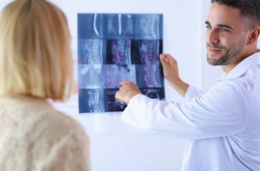 Yakışıklı doktor genç bayan hastasıyla konuşuyor ve ofisinde otururken notlar alıyor..