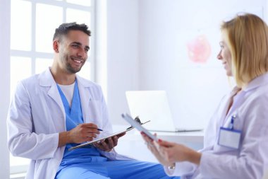 Yakışıklı doktor genç bayan doktorla konuşuyor ve ofisinde otururken notlar alıyor..