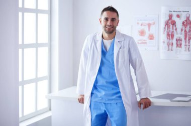 Genç ve kendinden emin erkek doktor portresi tıp ofisinde duruyor..