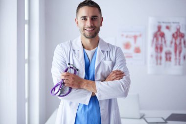 Genç ve kendinden emin erkek doktor portresi tıp ofisinde duruyor..