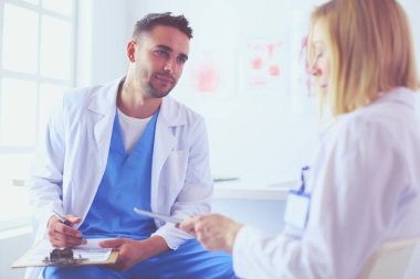 Yakışıklı doktor genç bayan doktorla konuşuyor ve ofisinde otururken notlar alıyor..
