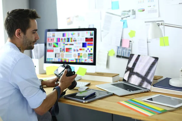 Retrato del joven diseñador sentado en el estudio gráfico frente a la computadora portátil y el ordenador mientras trabaja en línea. — Foto de Stock