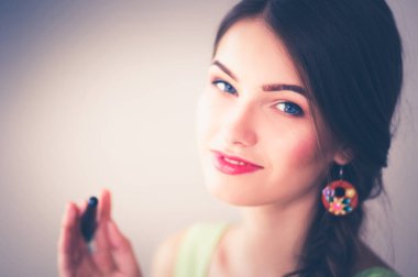 Gri duvarda gülümseyen genç bir kadının portresi.