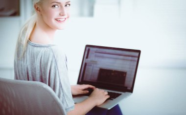 Genç ve güzel bir kadın evde dizüstü bilgisayar kullanıyor.