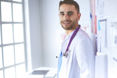 Genç ve kendinden emin erkek doktor portresi tıp ofisinde duruyor.