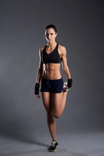 Muscular young woman posing in sportswear against black background. — Stock Photo, Image