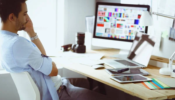 Porträt eines jungen Designers, der im Grafikstudio vor Laptop und Computer sitzt, während er online arbeitet. — Stockfoto