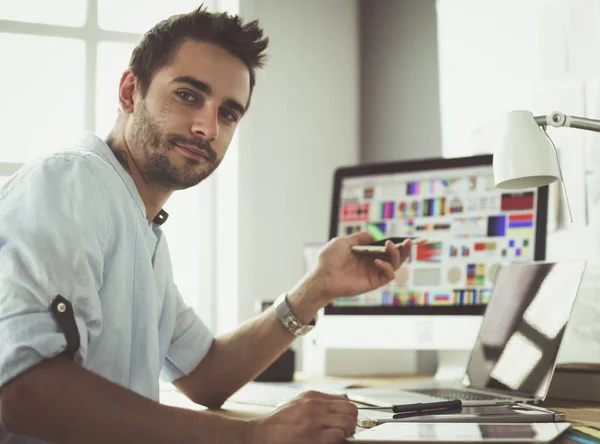 Portrait de jeune designer assis dans un studio graphique devant un ordinateur portable et un ordinateur tout en travaillant en ligne. — Photo