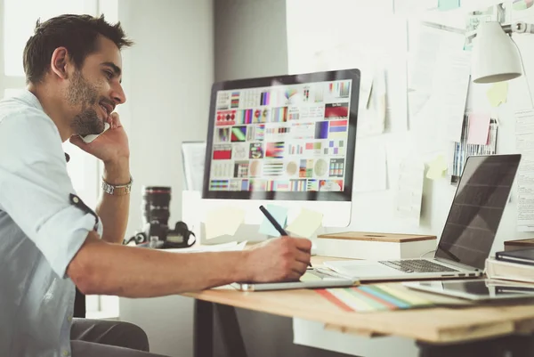 İnternette çalışırken bilgisayarın ve dizüstü bilgisayarın önünde grafik stüdyosunda oturan genç tasarımcının portresi.