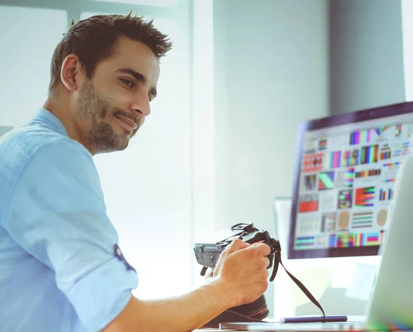 Retrato del joven diseñador sentado en el estudio gráfico frente a la computadora portátil y el ordenador mientras trabaja en línea. — Foto de Stock