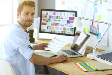 İnternette çalışırken bilgisayarın ve dizüstü bilgisayarın önünde grafik stüdyosunda oturan genç tasarımcının portresi.
