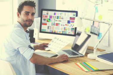 İnternette çalışırken bilgisayarın ve dizüstü bilgisayarın önünde grafik stüdyosunda oturan genç tasarımcının portresi.