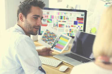 İnternette çalışırken bilgisayarın ve dizüstü bilgisayarın önünde grafik stüdyosunda oturan genç tasarımcının portresi.
