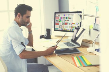 İnternette çalışırken bilgisayarın ve dizüstü bilgisayarın önünde grafik stüdyosunda oturan genç tasarımcının portresi.