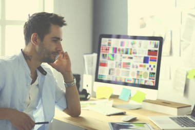 İnternette çalışırken bilgisayarın ve dizüstü bilgisayarın önünde grafik stüdyosunda oturan genç tasarımcının portresi.