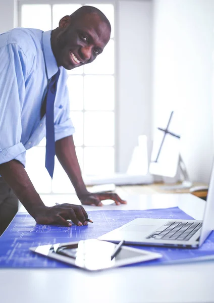 Afrikansk amerikansk arkitekt arbejder med computer og tegninger på kontoret - Stock-foto