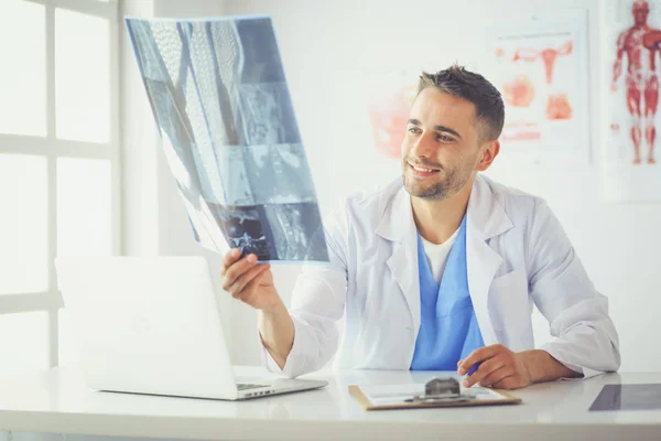 Joven doctor sentado en su escritorio de la oficina y analizando una radiografía — Foto de Stock