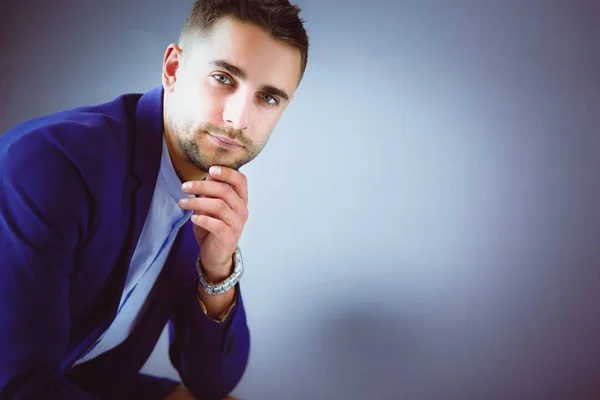 Young businessman sitting isolated on grey background — Stock Photo, Image