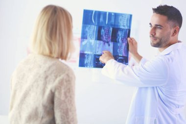 Yakışıklı doktor genç bayan hastasıyla konuşuyor ve ofisinde otururken notlar alıyor..